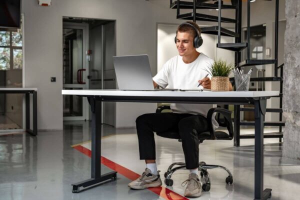 Mężczyzna pracuje przy laptopie siedząc przy biurku elektrycznym w nowoczesnym biurze.