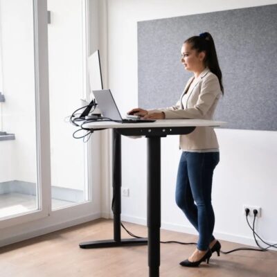 Kobieta pracuje przy komputerze, stojąc przy biurku regulowanym.